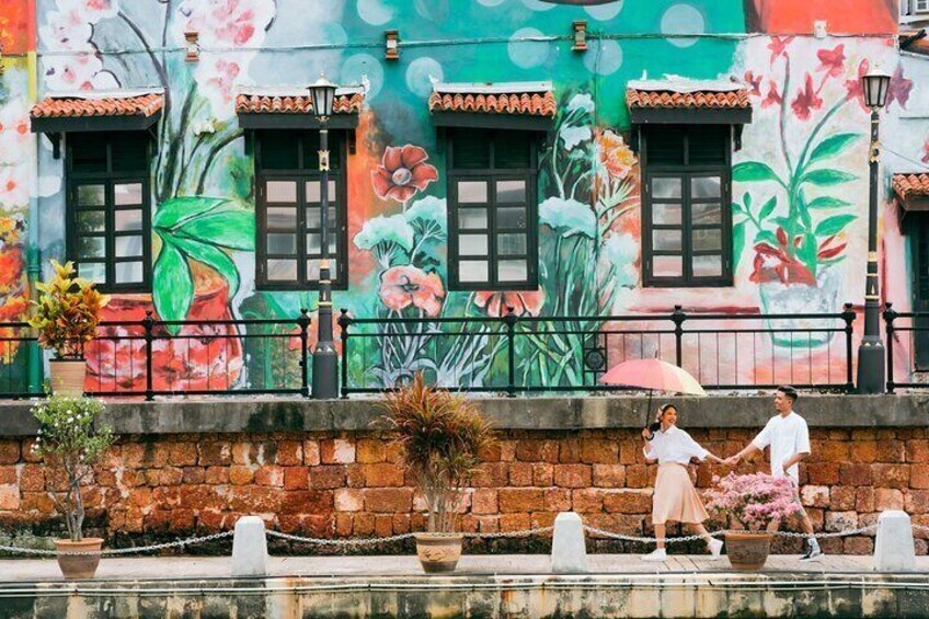 A couple holding hands walking along a canal with a colorful mural on the building behind them. 5