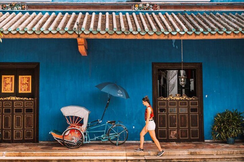 Iemand loopt langs een blauw gebouw met traditionele deuren en een fiets met een witte afdekking. 5
