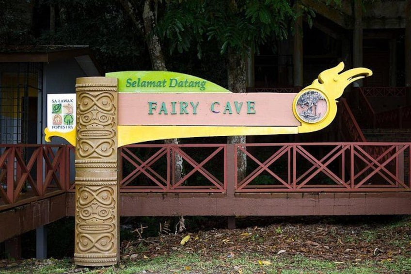 A sign for 'Fairy Cave' with a decorative design and a bridge in the background. 1