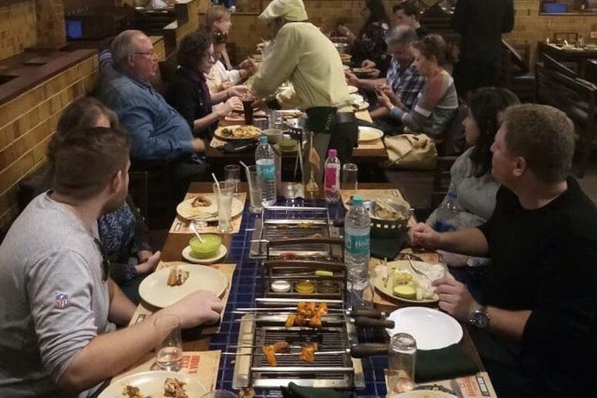 A group of people dining at a restaurant with a long communal table, various dishes, and a grill in the center. 3