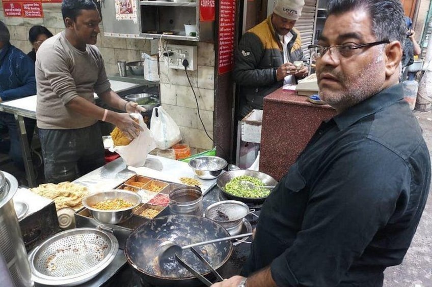A street food vendor preparing food at a stall with various cooking utensils and ingredients visible. 4