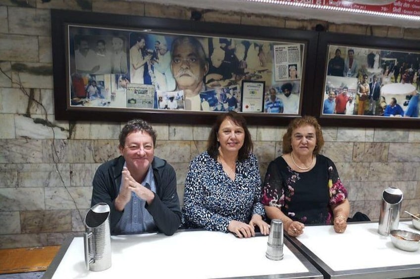 Three people seated at a table with a framed collage of photographs on the wall behind them. 5