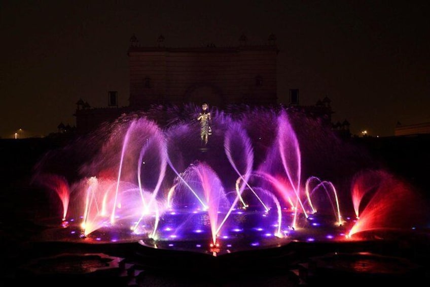 A nighttime fountain display with water jets illuminated in purple and red lights. 1