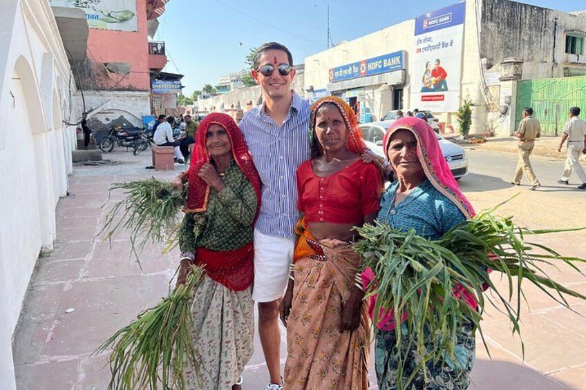 Three people standing on a street, holding bundles of green plants. In the background, there are buildings, including a bank with a sign that reads 'HDFC BANK'. 5