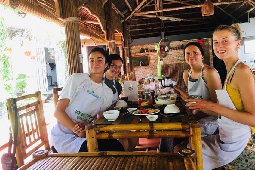 Cuatro personas en una mesa de madera con comida y utensilios de cocina, en un entorno rústico al aire libre. 5