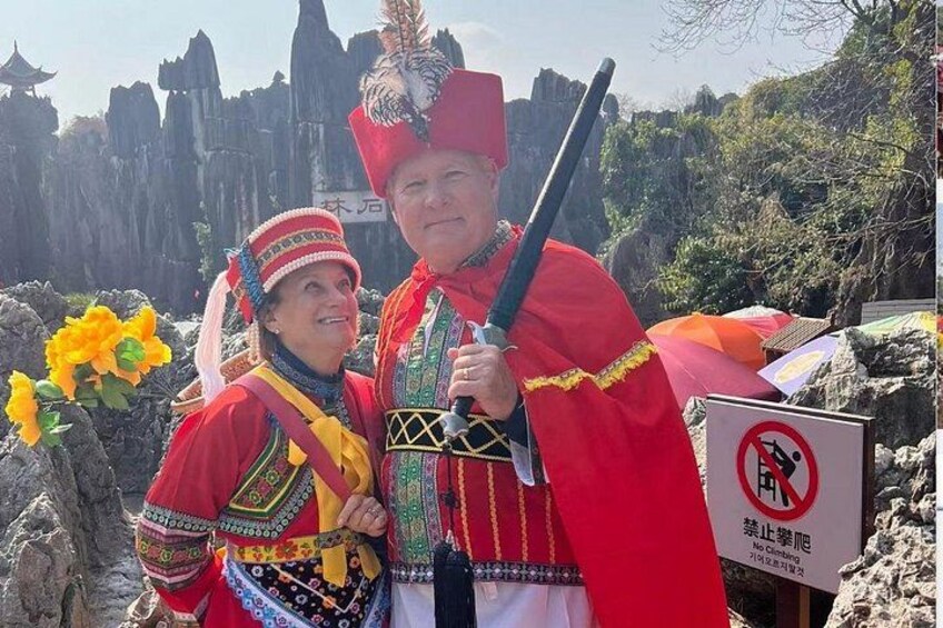 Two people in traditional attire with a mountainous background and a no-climbing sign. 1