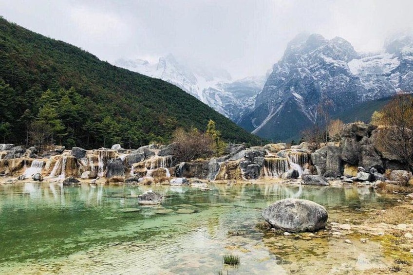 Paesaggio montuoso con un fiume limpido, affioramenti rocciosi e cime innevate sullo sfondo. 5