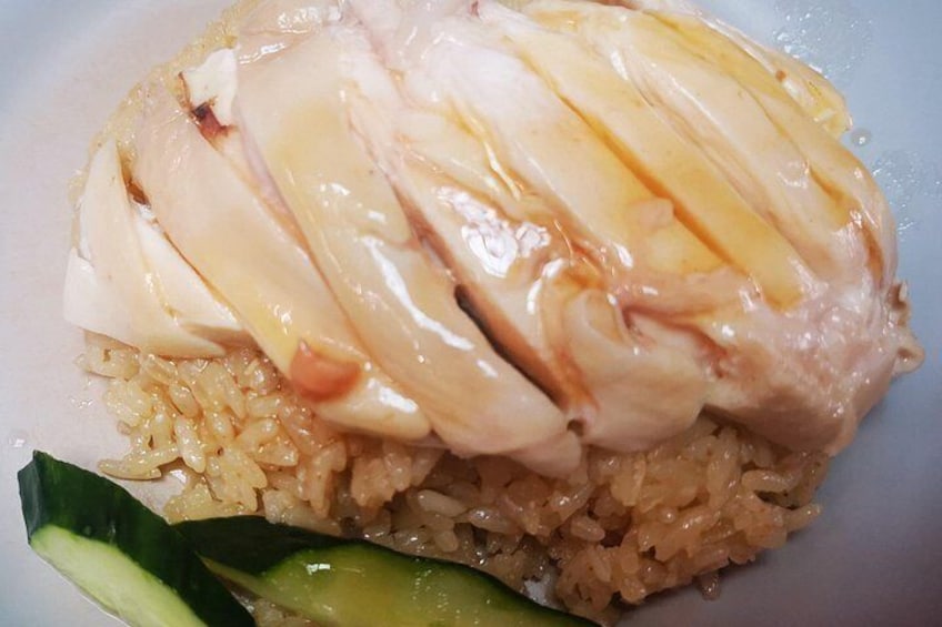 A plate of food with rice, chicken, and a cucumber slice. 2