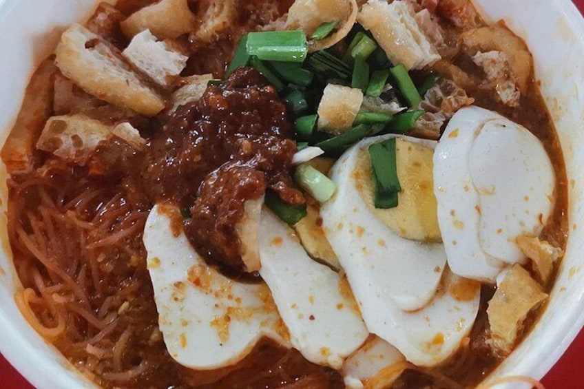 A bowl of noodle soup with sliced eggs, green onions, and a dark sauce. 4