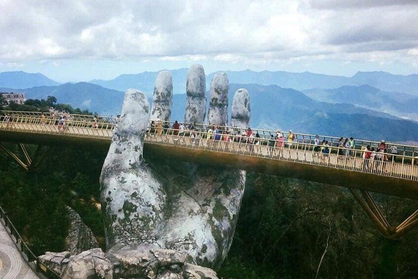A bridge with a large hand-like structure underneath, surrounded by mountains. 2