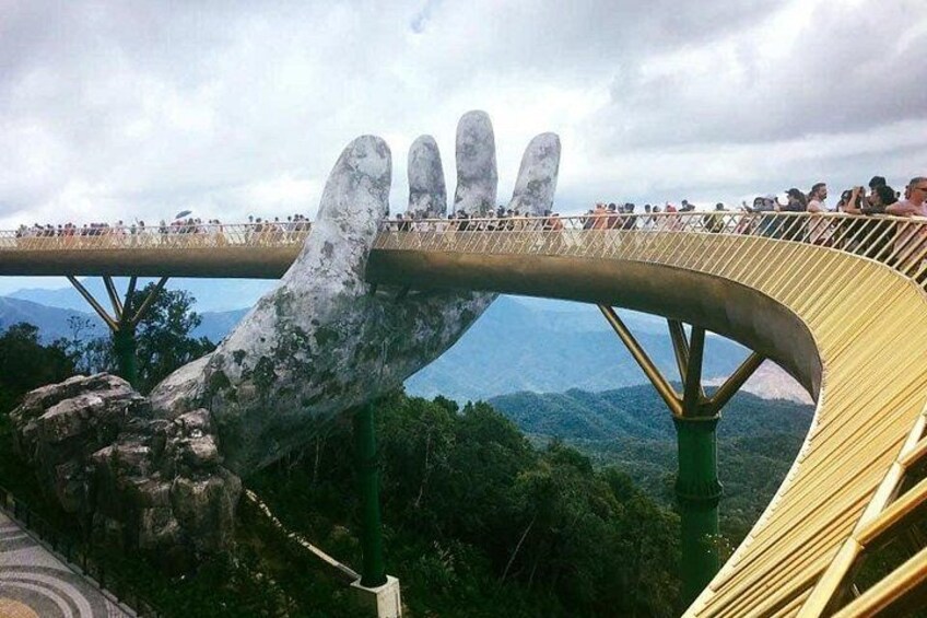 A large hand sculpture supporting a bridge with people walking on it. 3