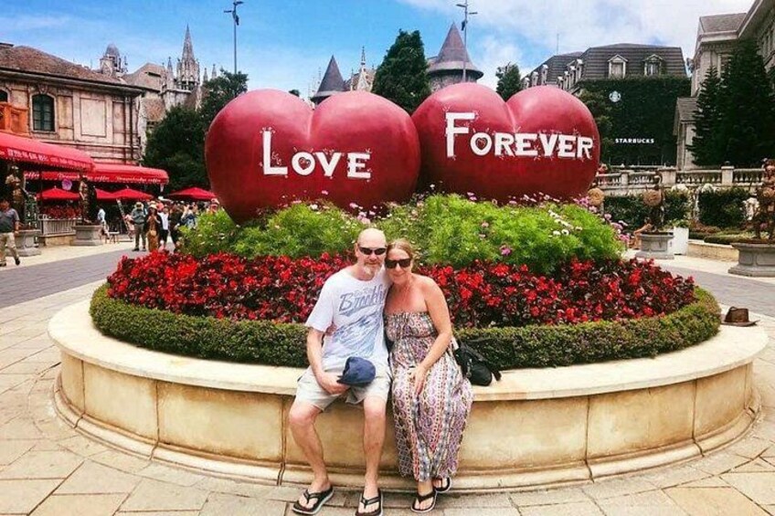 A couple sitting in front of a heart-shaped flower bed with the words 'Love Forever' on it. 4