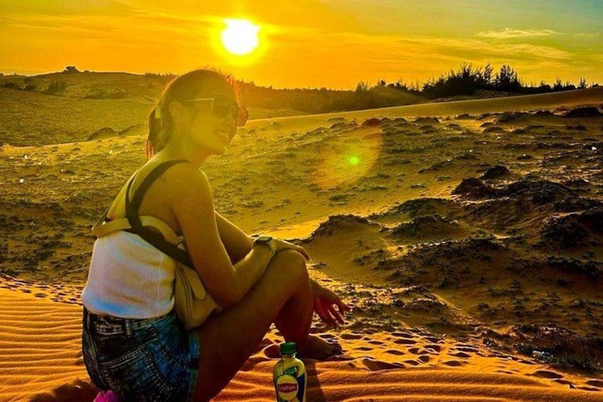 A person sitting on a sandy beach at sunset with a bottle of water. 3