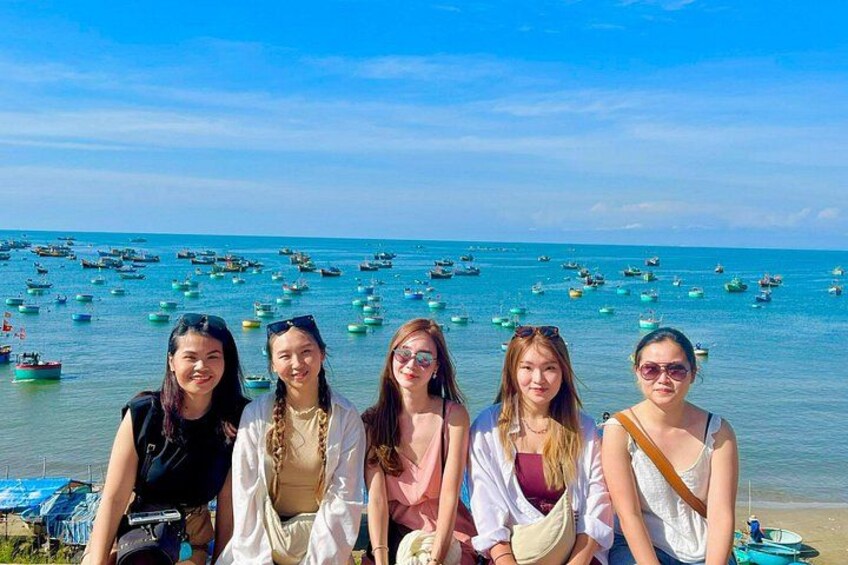 A group of people sitting on a beach with a view of the sea and numerous boats. 4