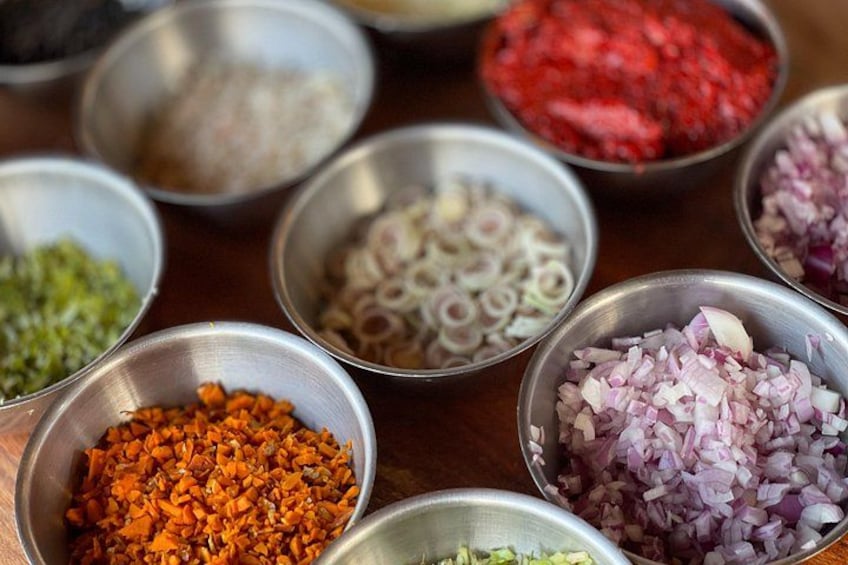 Various ingredients in metal bowls, including chopped onions, red chili powder, and other spices. 5