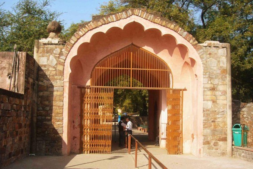 A stone archway with a metal gate, a person standing in the background, and a green trash bin to the right. 5