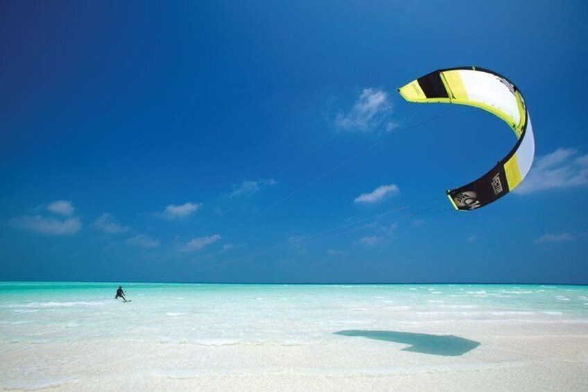 A person parasailing over a beach with clear turquoise water. 3