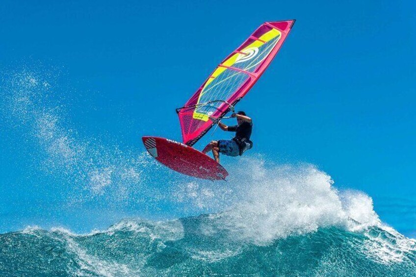 A person windsurfing on a large wave with a colorful sail. 2