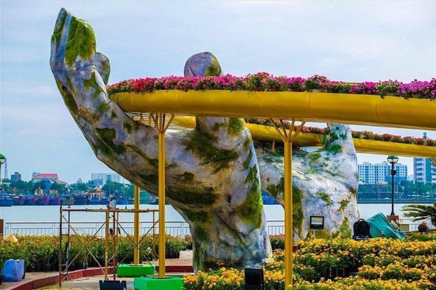 A large sculpture of a hand holding a flower pot, with a river and buildings in the background. 2