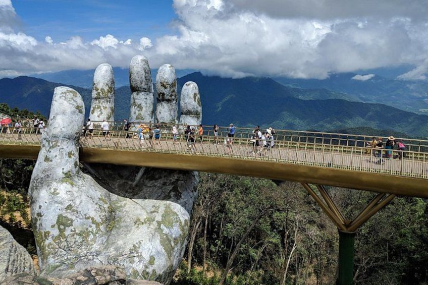 A bridge with a large hand sculpture, people walking, and a mountainous landscape. 5