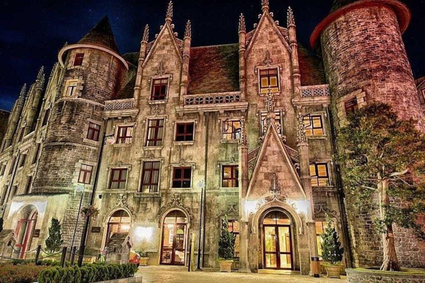 A large, historic building with multiple towers and arched windows, illuminated at night. 3
