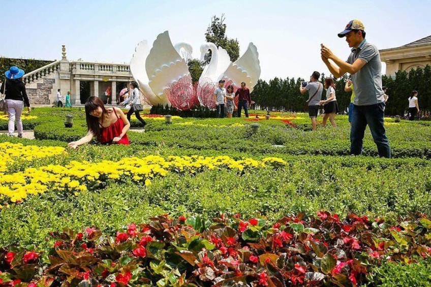 A garden with yellow and red flowers, a large white sculpture, and people walking around. 3