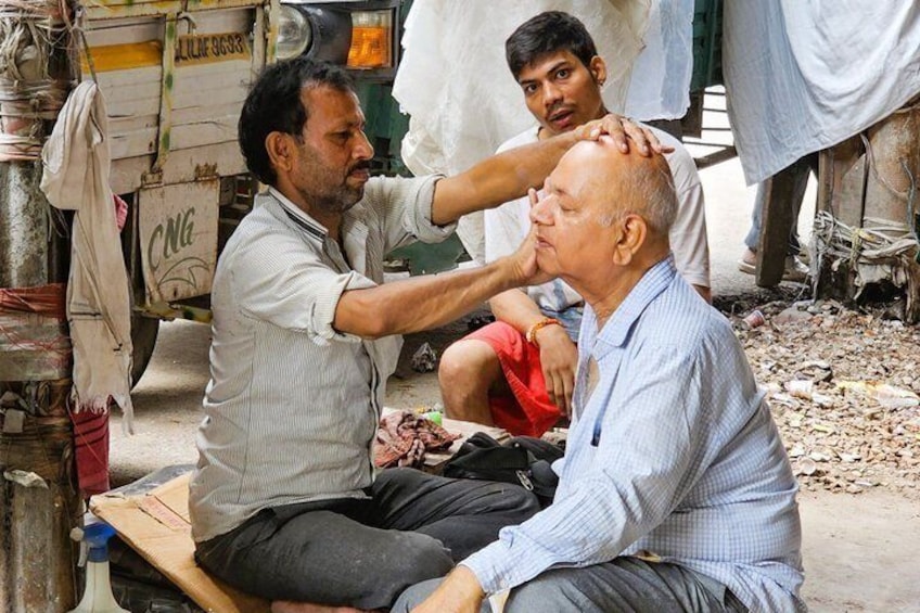 Two men sitting on a wooden bench outdoors, one receiving a head massage from another man. 3