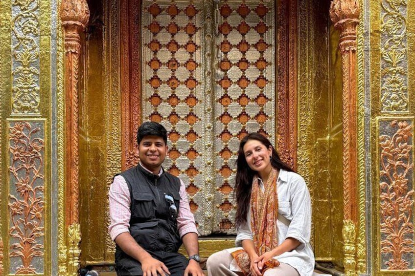Two people sitting in front of ornate golden and orange patterned architecture. 1