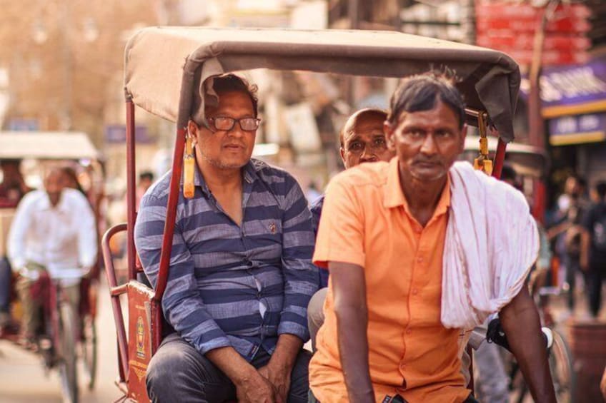 A man in a striped shirt and another in an orange shirt on a rickshaw. 5