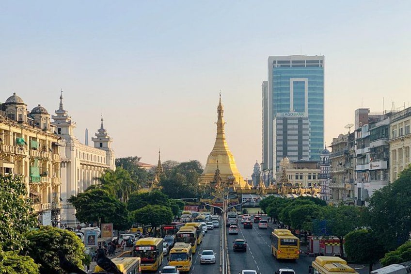 A busy urban street with a prominent golden stupa in the center, surrounded by modern buildings and traffic. 5