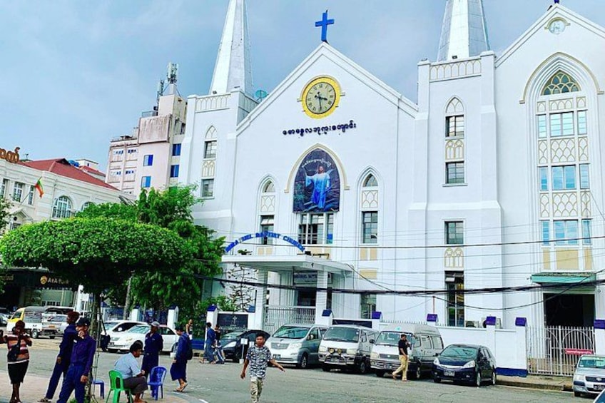 A white church with a cross and a clock on the front. There are people walking in front and cars parked nearby. 4