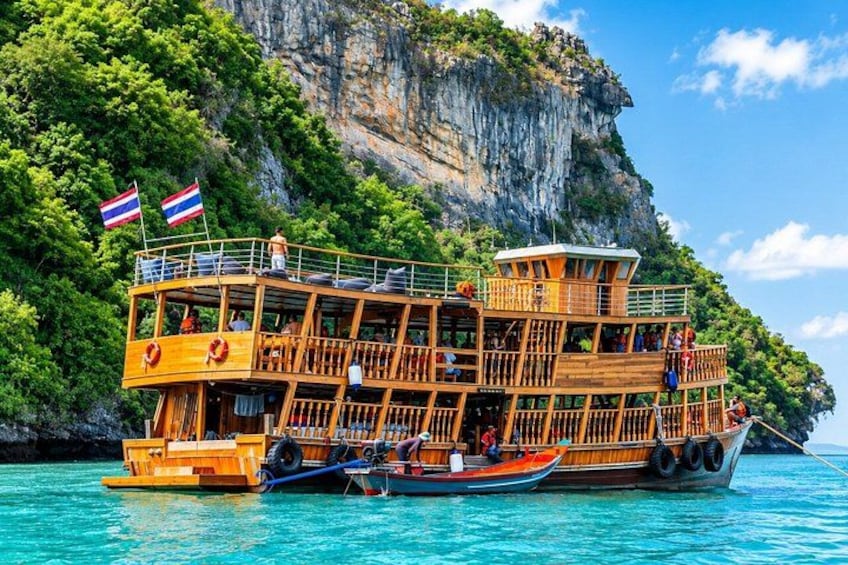 A wooden boat with multiple decks, flags, and a rocky cliff in the background. 2