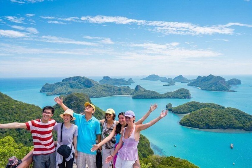 A group of people taking a selfie with a scenic view of a coastal landscape with islands and clear blue waters. 2