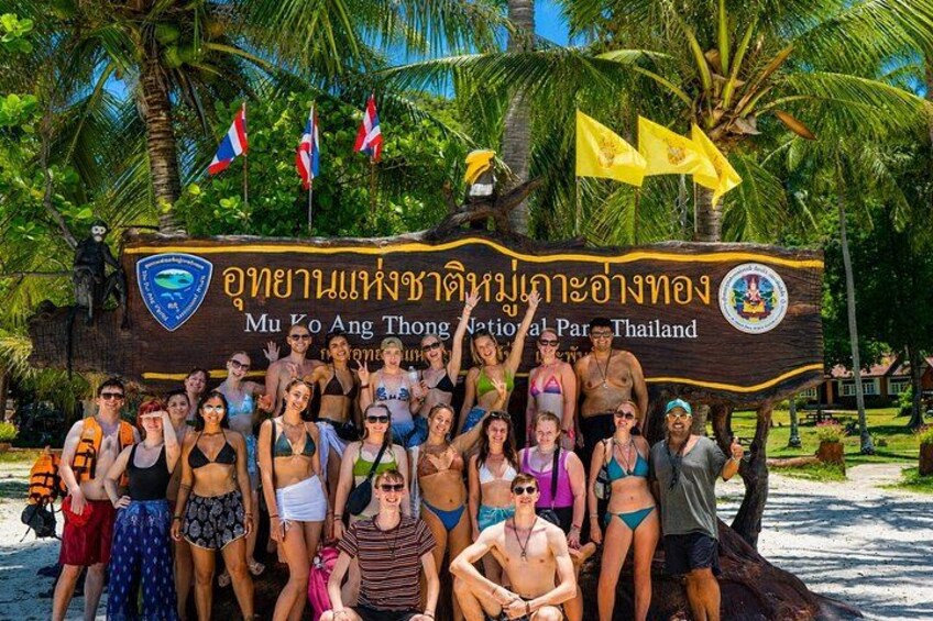 A group of people posing in front of a sign with Thai text and flags. 4