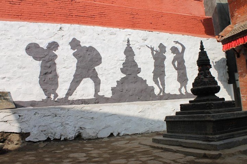 A wall with a relief sculpture of figures, a brick wall, and a small black structure. 1