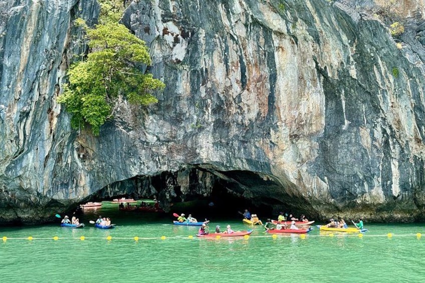 A group of people kayaking near a large rock formation with a cave entrance. 3