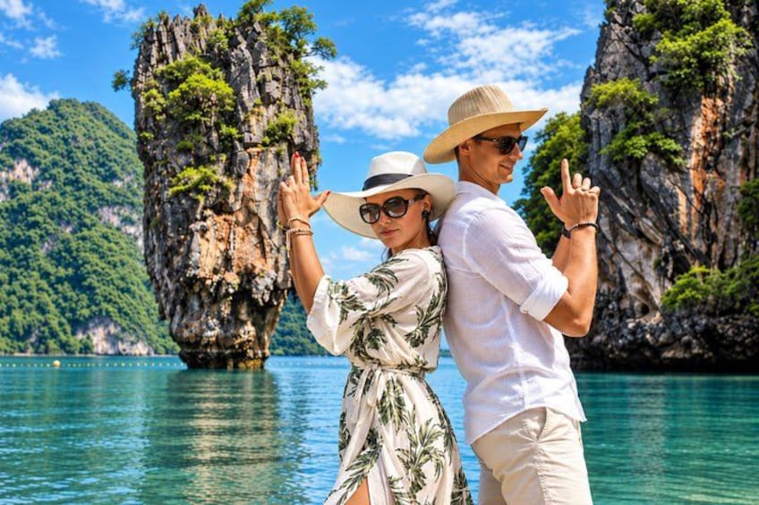 A couple standing by a rocky coastline with clear water and greenery. 1