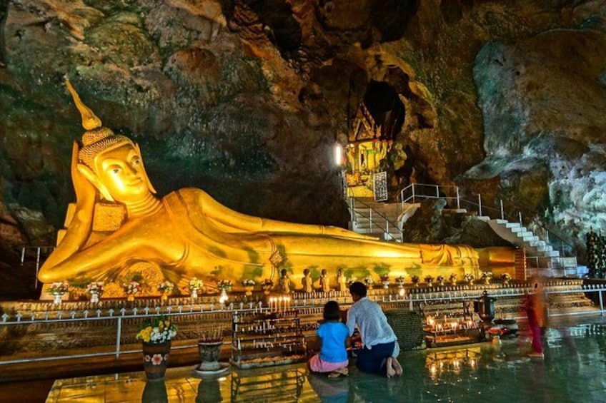 A large golden reclining Buddha statue in a cave, with stairs leading up to it and people visiting. 3