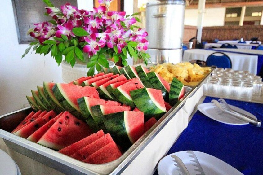 Une table de buffet avec des tranches de pastèque, un arrangement floral et un récipient contenant des condiments. 5