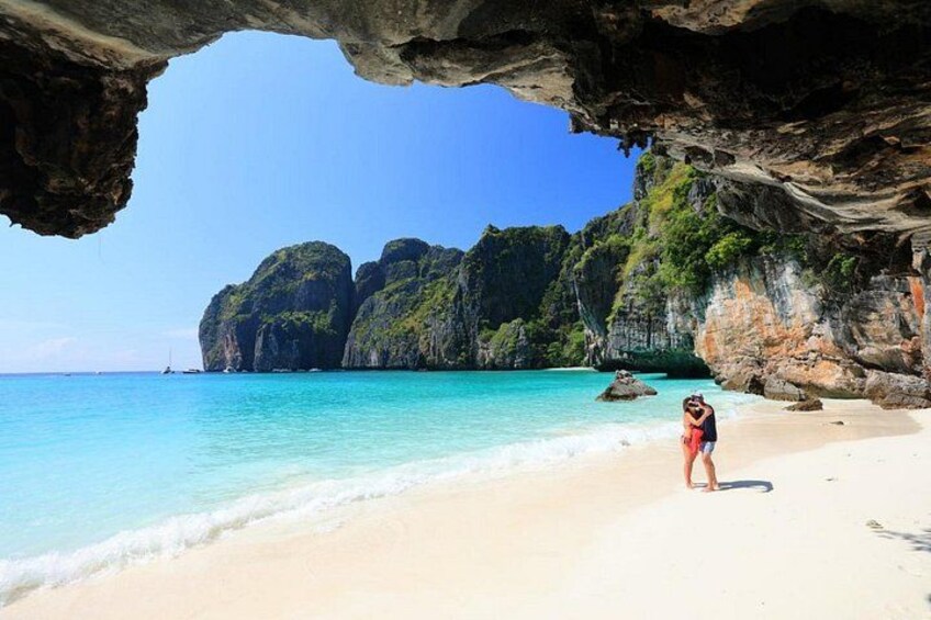 Une plage à l’eau turquoise et limpide, une personne debout sur le sable et, au loin, de grandes formations rocheuses. 4