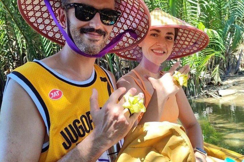 Een persoon in een geel tanktop met de tekst 'JUGO', vasthoudend een gele bloem, en een ander persoon in een gele jurk met een grote rode en paarse hoed. 4