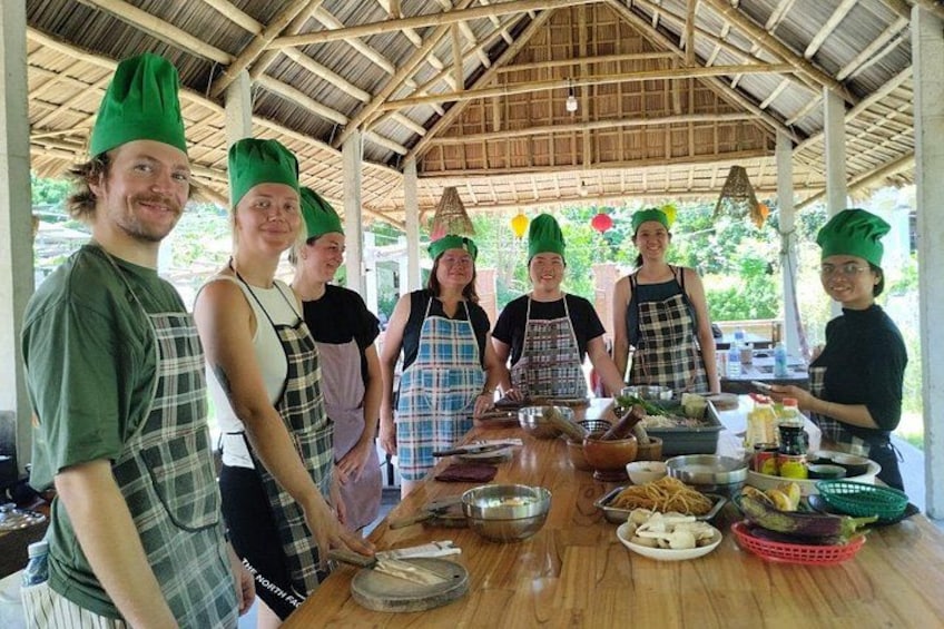 Een groep mensen met koksmutsen en schorten staat rond een tafel met keukengerei en ingrediënten. 3
