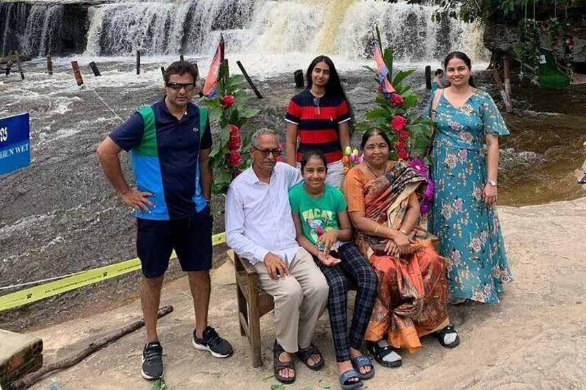 A group of people posing in front of a waterfall with a sign that reads 'CHEN WET.' 3