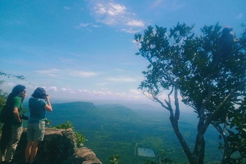 Dos personas de pie en un acantilado con vista a un valle, con un árbol en primer plano. 2