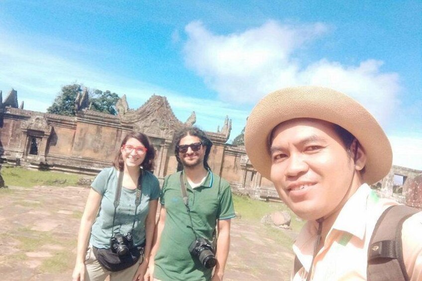 Drei Personen vor einem antiken Tempel mit Steinmetzarbeiten und blauem Himmel. 5