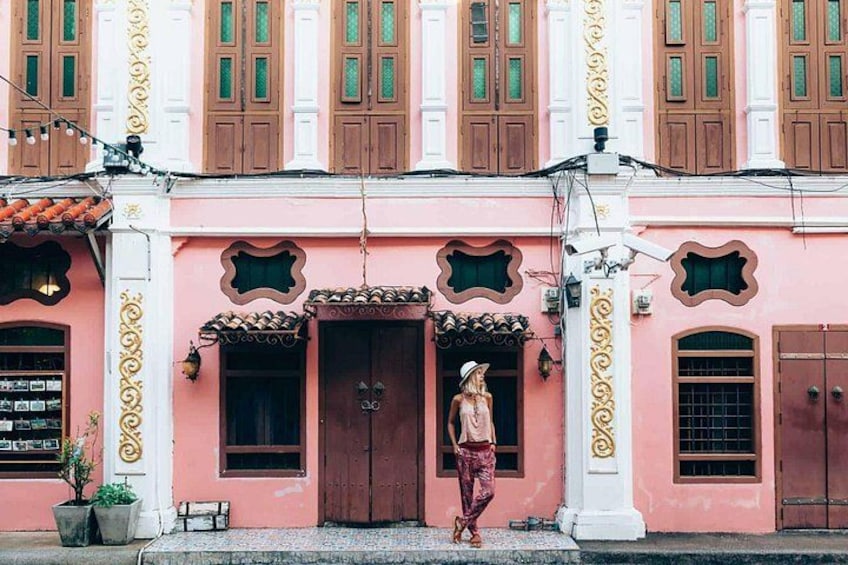 Un bâtiment rose orné de décorations élaborées, une femme portant un pantalon à motifs et une plante en pot. 3