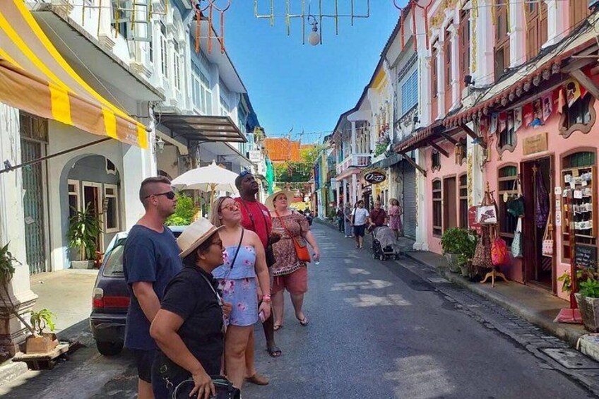 A narrow street lined with colorful buildings, a parked car, and people walking. 3