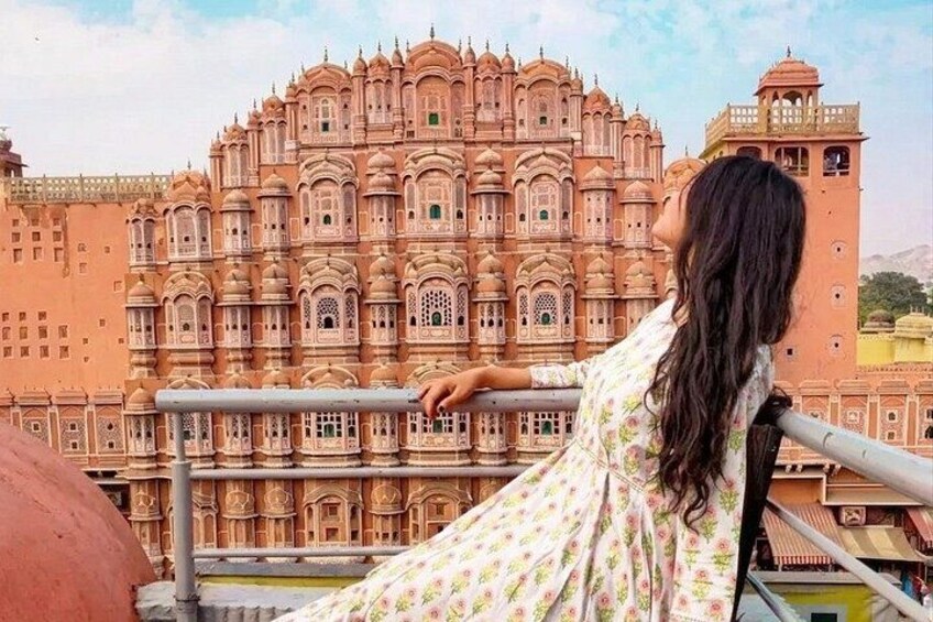A person standing on a balcony overlooking a large, ornate building with intricate architecture. 1