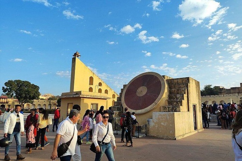 A crowded square with a large circular monument and a yellow building with a bell tower. 5