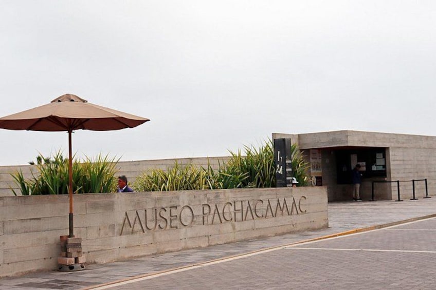 De ingang van een museum, met een bord waarop 'Museo Pachacamac' staat en een betonnen muur met beplanting. 5